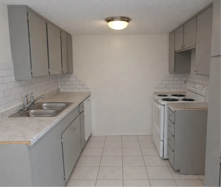 A clean galley kitchen with grey cabinetry, white subway tile backsplash, and tile flooring at La Villa Elms Apartments.