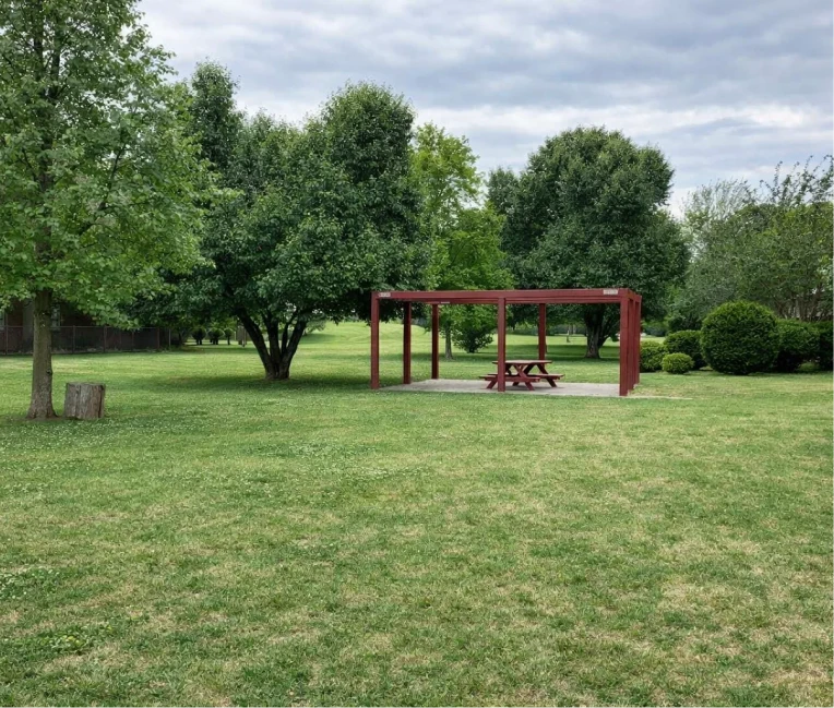 Outdoor picnic table under a red wooden pergola on the grassy grounds of La Villa Elms Apartments.