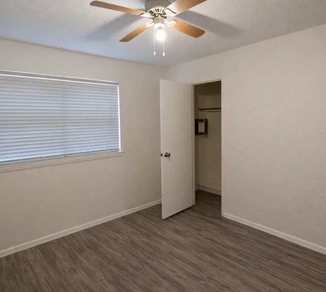 Bright apartment bedroom with wood-style flooring, a ceiling fan, and a walk-in closet, located minutes from downtown Oklahoma City.