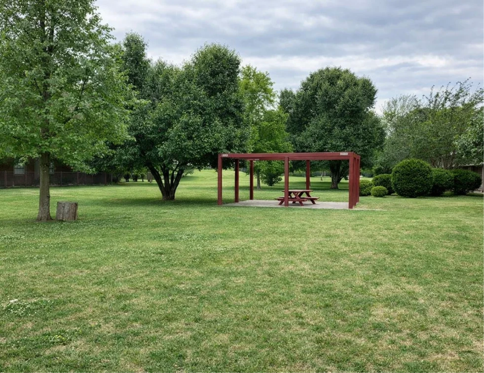 Shaded red picnic area and lush green lawn at La Villa Elms, offering utilities included apartments El Reno.