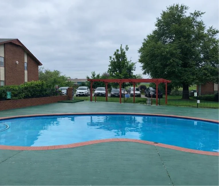 Blue curved swimming pool with a red pergola and lounge area at apartments with pool El Reno.