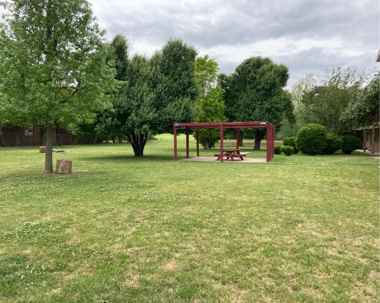 Vibrant green courtyard with a shaded red picnic pergola at La Villa Elms, planted in the heart of El Reno.