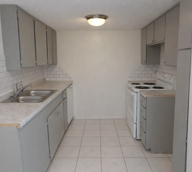 Renovated galley kitchen with grey cabinets and white subway tile at La Villa Elms, located near top shopping and dining in El Reno.
