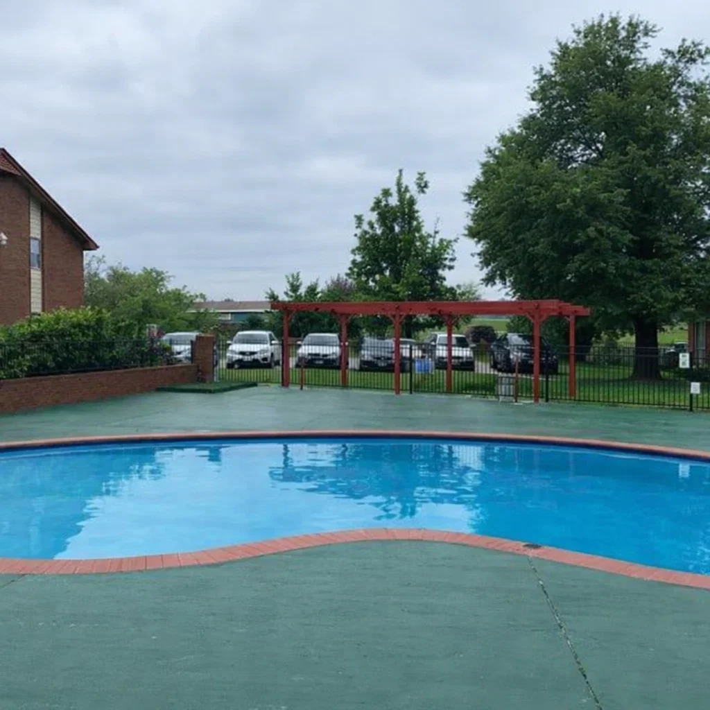 Outdoor swimming pool with brick trim and a red pergola at Oklahoma City apartments in El Reno.